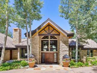Experience luxury mountain living in this stunning stone-clad residence, featuring a grand double-door entrance framed by towering aspen trees.