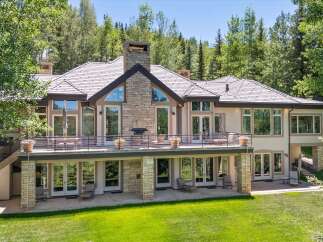 Experience luxury mountain living in this stunning estate, featuring a grand stone facade and expansive windows that capture breathtaking forest views.
