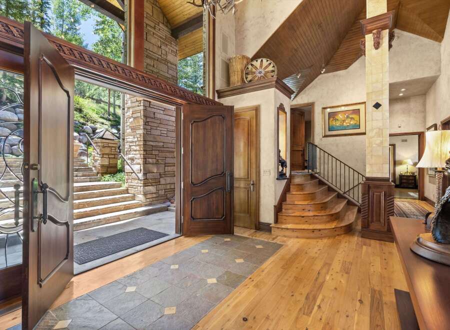 Step into a grand entryway featuring a stunning double door opening to a stone staircase and lush greenery.