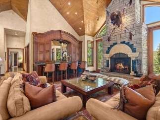 Experience rustic luxury in this grand living room, featuring a stunning stone fireplace with a mounted bison head and a full-service wooden bar with leather stools.
