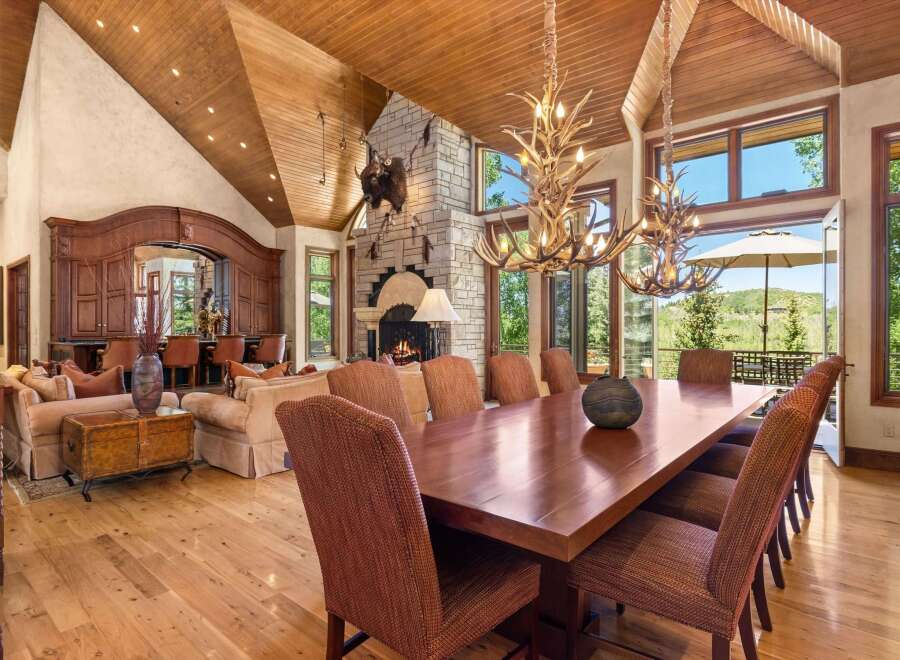 Experience luxurious mountain living in this grand dining room, featuring a massive stone fireplace and a rustic antler chandelier.