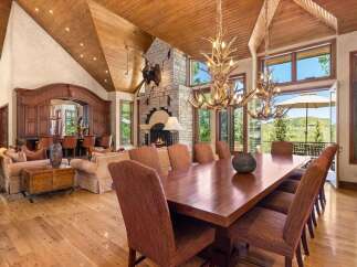 Experience luxurious mountain living in this grand dining room, featuring a massive stone fireplace and a rustic antler chandelier.
