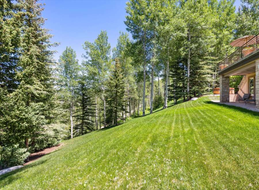 Experience the beauty of nature with this stunning property, featuring a lush green lawn that slopes gently towards a serene wooded area.