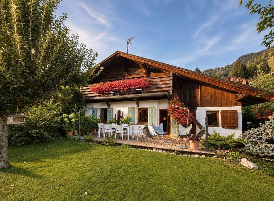 Experience alpine charm in this picturesque wooden chalet, featuring a spacious balcony adorned with vibrant red flowers and a welcoming outdoor dining area.