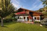 Experience alpine charm in this picturesque wooden chalet, featuring a spacious balcony adorned with vibrant red flowers and a welcoming outdoor dining area.