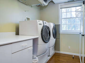 This laundry room features a modern design with a sleek white countertop and cabinetry, providing ample space for folding and storage.