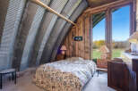 Experience unique living in this charming bedroom featuring a rustic corrugated metal arched ceiling and warm wooden walls.
