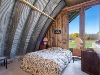 Experience unique living in this charming bedroom featuring a rustic corrugated metal arched ceiling and warm wooden walls.