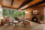 Experience mid-century modern charm in this inviting living room, featuring a stunning wood-paneled beamed ceiling and a cozy brick fireplace.