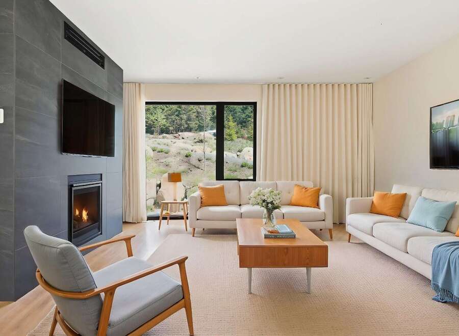 Experience modern living in this stunning living room, featuring a sleek fireplace with an integrated TV and a large window offering breathtaking natural views.