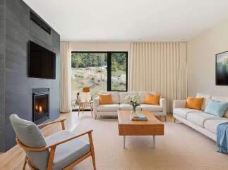 Experience modern living in this stunning living room, featuring a sleek fireplace with an integrated TV and a large window offering breathtaking natural views.