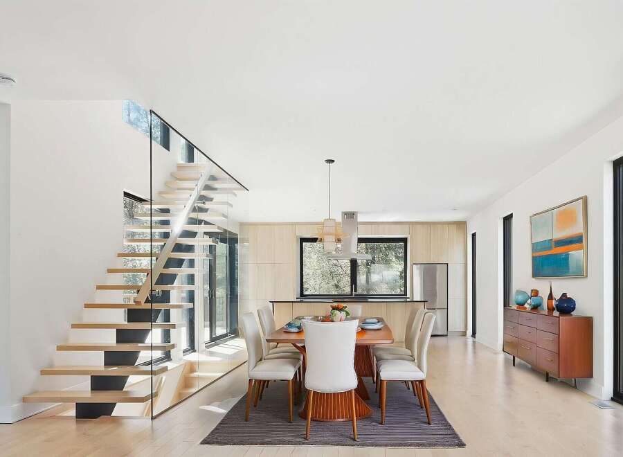 Experience modern living in this stunning home featuring a floating staircase with glass railings and an open-concept dining and kitchen area.