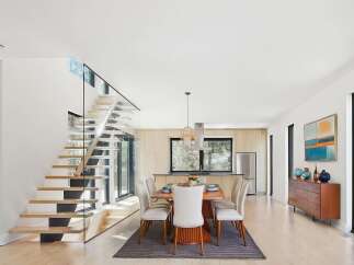 Experience modern living in this stunning home featuring a floating staircase with glass railings and an open-concept dining and kitchen area.