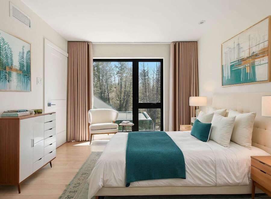 Experience modern luxury in this serene bedroom, featuring a plush king-sized bed adorned with crisp white linens and accented by a vibrant teal throw.