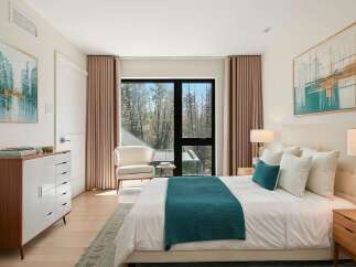 Experience modern luxury in this serene bedroom, featuring a plush king-sized bed adorned with crisp white linens and accented by a vibrant teal throw.