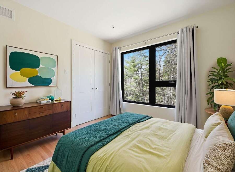 This bedroom offers a serene retreat with its large window overlooking a lush forest, bringing the outdoors in.