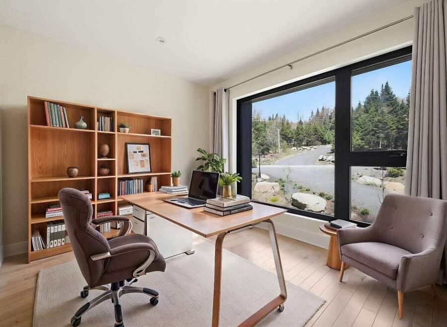 This modern home office features a large wooden desk with a laptop and books, complemented by a comfortable upholstered chair.
