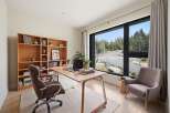 This modern home office features a large wooden desk with a laptop and books, complemented by a comfortable upholstered chair.