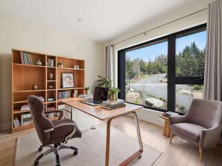 This modern home office features a large wooden desk with a laptop and books, complemented by a comfortable upholstered chair.