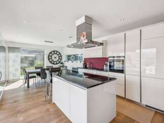 This modern kitchen boasts sleek white cabinetry and a spacious island with a black countertop, perfect for meal preparation and casual dining.
