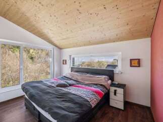 This cozy bedroom features a unique wooden ceiling and large windows that offer stunning views of the surrounding landscape.