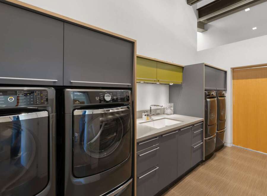 This modern laundry room features a sleek design with dark gray cabinetry and a contrasting lime green accent cabinet above the sink.