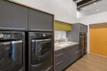 This modern laundry room features a sleek design with dark gray cabinetry and a contrasting lime green accent cabinet above the sink.