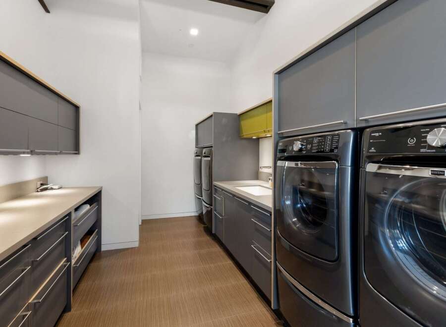 This modern laundry room boasts sleek, dark gray cabinetry and countertops, offering ample storage and a clean aesthetic.