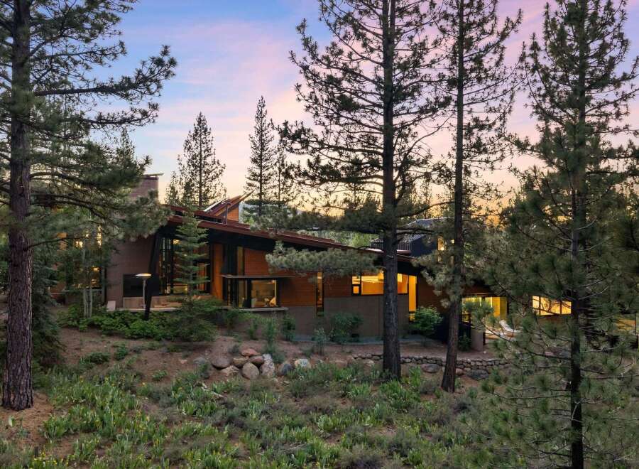Nestled amongst towering pine trees, this architectural gem boasts a striking modern design with a sloped roof and expansive glass windows.
