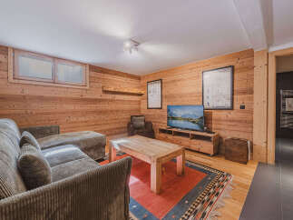 Experience cozy living in this charming mountain retreat, featuring warm wood-paneled walls and a comfortable sectional sofa perfect for relaxing after a day of skiing.
