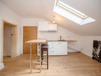 Discover this charming attic apartment featuring a modern kitchenette with sleek white cabinetry and a convenient breakfast bar.