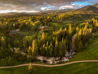 Experience luxury living nestled amidst a pristine mountain landscape, featuring a stunning modern home with expansive windows overlooking a vibrant forest and a rushing river.