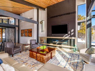 Experience luxury mountain living in this stunning contemporary home, featuring a grand living room with soaring ceilings and exposed wooden beams.