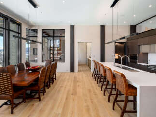 Experience luxury living in this spacious open-concept dining and kitchen area, featuring a large wooden dining table with plush leather chairs and a modern kitchen island with bar seating.
