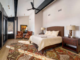 Experience luxury mountain living in this stunning bedroom featuring a plush king-sized bed, elegant upholstered accent chairs, and a large area rug with intricate patterns.