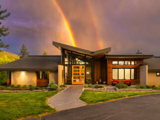 Experience luxury living in this stunning modern home, perfectly situated against a dramatic sky with a double rainbow.