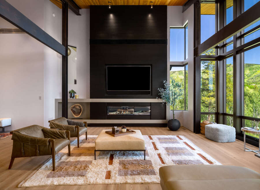 Experience luxury living in this stunning modern living room, featuring a dramatic floor-to-ceiling fireplace and expansive windows that showcase breathtaking mountain views.