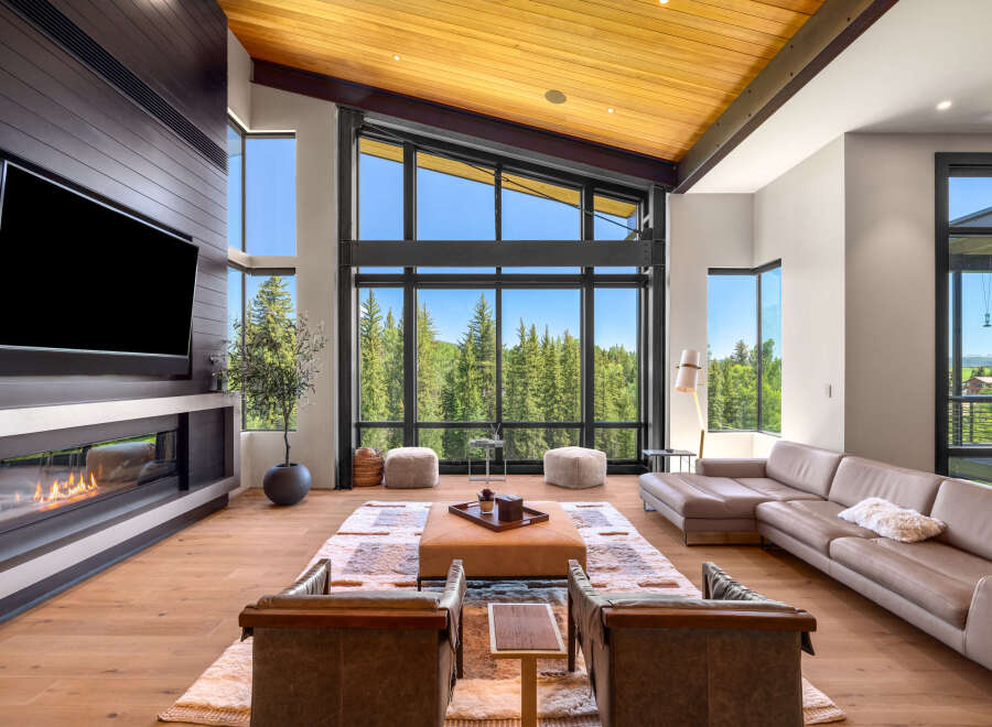 Experience luxury mountain living in this stunning great room, featuring a modern fireplace and expansive floor-to-ceiling windows that showcase breathtaking forest views.