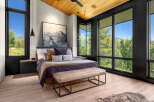 Experience luxury mountain living in this stunning bedroom featuring a vaulted wood-paneled ceiling and expansive windows that frame breathtaking forest and mountain views.