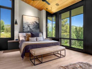 Experience luxury mountain living in this stunning bedroom featuring a vaulted wood-paneled ceiling and expansive windows that frame breathtaking forest and mountain views.