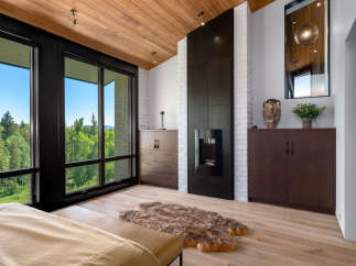Experience luxury living with this stunning bedroom featuring a modern fireplace and expansive windows offering breathtaking forest views.