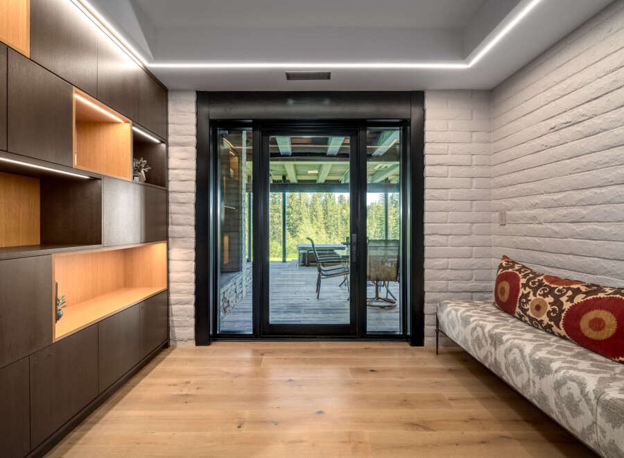 Experience seamless indoor-outdoor living with this stunning room featuring a modern built-in dark wood shelving unit with integrated lighting.