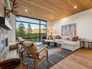 Experience luxurious mountain living in this stunning great room, featuring a floor-to-ceiling stone fireplace and expansive windows that frame breathtaking forest views.