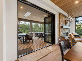 Experience seamless indoor-outdoor living with expansive bi-fold doors opening onto a covered deck, perfect for enjoying the surrounding forest views.