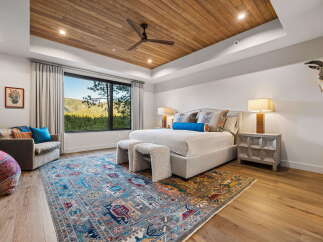 Experience luxury mountain living in this stunning bedroom featuring a vaulted wood-paneled ceiling and a large picture window with breathtaking views.