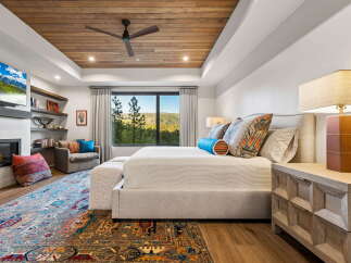 Experience luxury mountain living in this stunning master bedroom, featuring a cozy fireplace, a large flat-screen TV, and a plush king-sized bed.