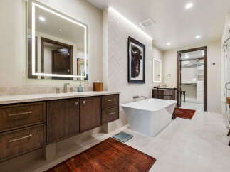Experience luxury in this stunning bathroom featuring a freestanding soaking tub, a modern vanity with ample storage, and a large, illuminated mirror.