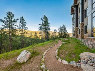 Discover this stunning property nestled amidst a serene landscape, featuring a winding gravel path bordered by natural stones, leading towards a modern building with stone accents.