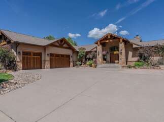 This stunning home boasts a grand entrance with a covered porch supported by stone pillars and a wooden beamed ceiling.