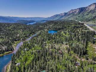 Discover this stunning aerial view showcasing a serene landscape with a winding river, a tranquil lake, and a dense forest dotted with charming cabins.